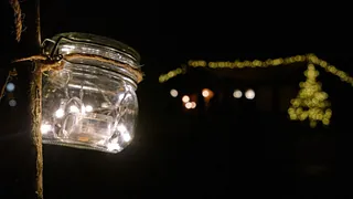 Weckglas mit Lichterkette im Klostergarten, im Hintergrund Lichterketten an Bäumen