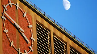 Blick auf die Uhr am Kirchturm, rechts seitlich ist der Halbmond vor blauem Himmel zu sehen