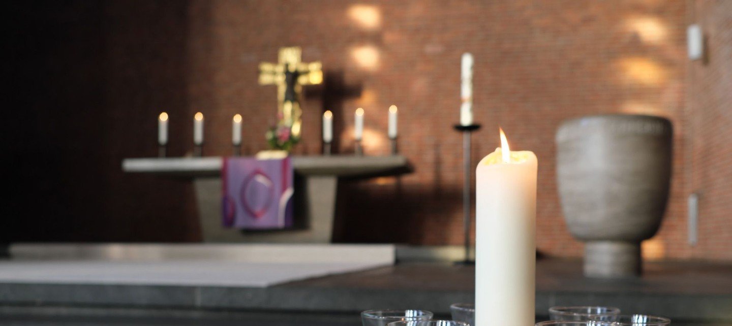 Nahaufnahme einer angezündeten Kerze, im Hintergrund der Altar der Martin-Luther-Kirche