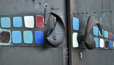 Nahaufnahme der Türgriffe in Fischform an der Kirchentür vor blauen und roten Emaile Platten