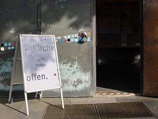 Offene Kirchentür mit einem Hinweisschild zur Öffnung