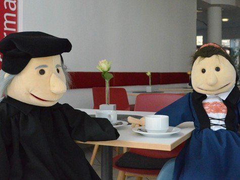 Die Handpuppen Käthe von Bora und Martin Luther sitzen am Kaffeetisch im Foyer