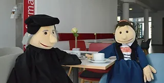 Die Handpuppen Käthe von Bora und Martin Luther sitzen am Kaffeetisch im Foyer