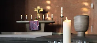 Weiße dicken brennende Kerze, im Hintergrund ist der Altar